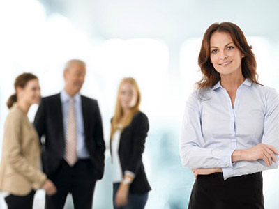 Eine Frau steht im Vordergrund, während drei Personen im Hintergrund unscharf diskutieren.